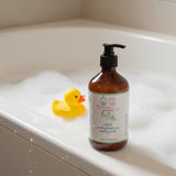 A bottle of Rebecca's Baby natural soothing red-to-toe cleansing wash, in an amber brown bottle with a black pump dispenser and a white label, set against a plain white background.