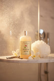 A bottle of Rebecca's Paradise Soft and Dreamy Vanilla Bean Body Wash, featuring a translucent pale peach-colored bottle with a silver cap and cream label, set against a plain white background.